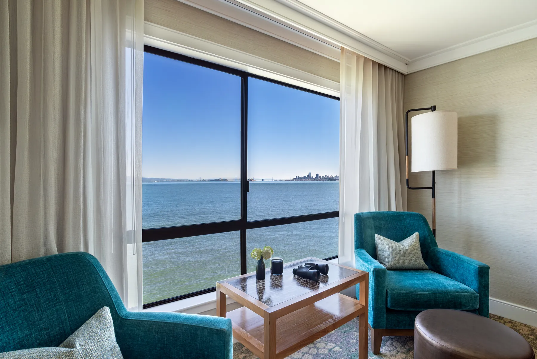 Window seating area with teal armchairs framing a view of the San Francisco skyline over the bay