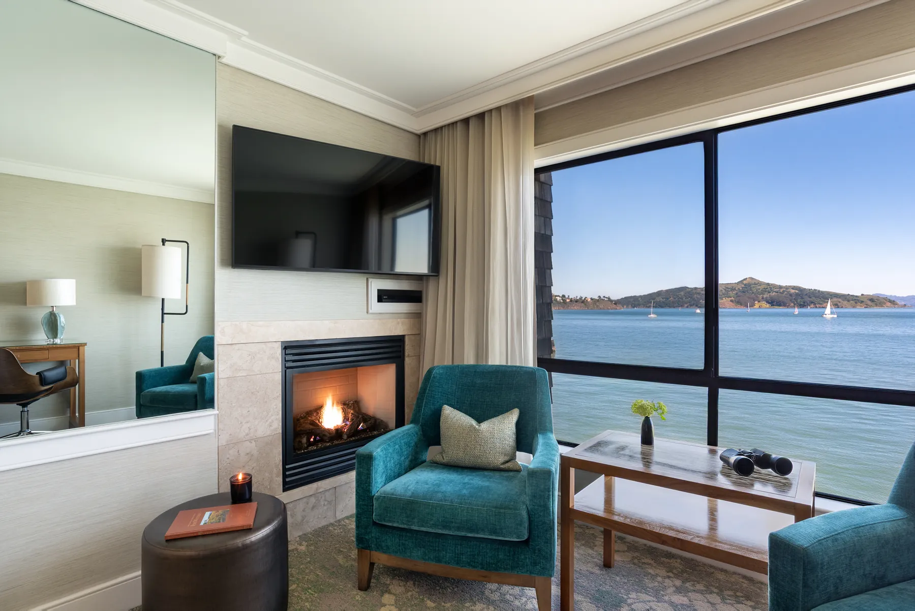 Guest suite sitting area at this Sausalito hotel with fireplace, teal armchairs and bay view of Angel Island
