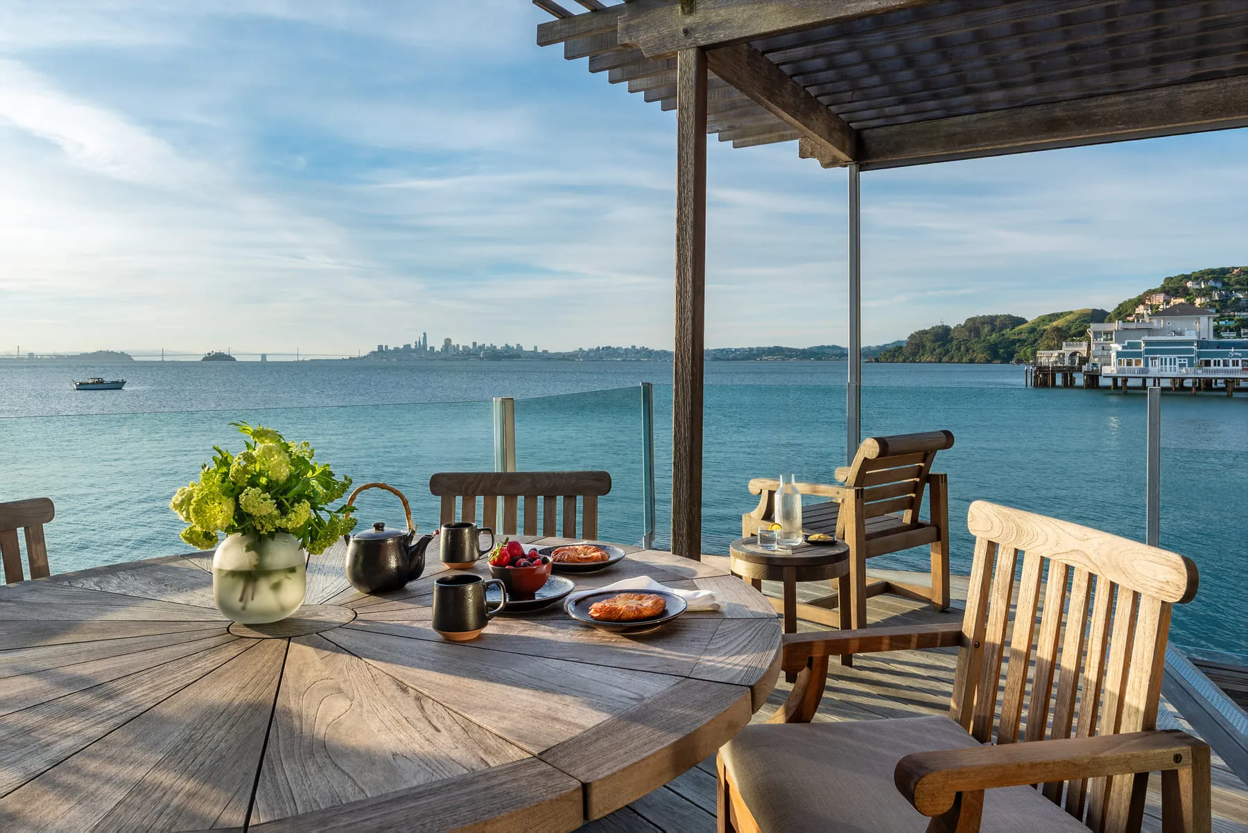 Breakfast for two on a teak table on a deck overlooking the bay and city skyline