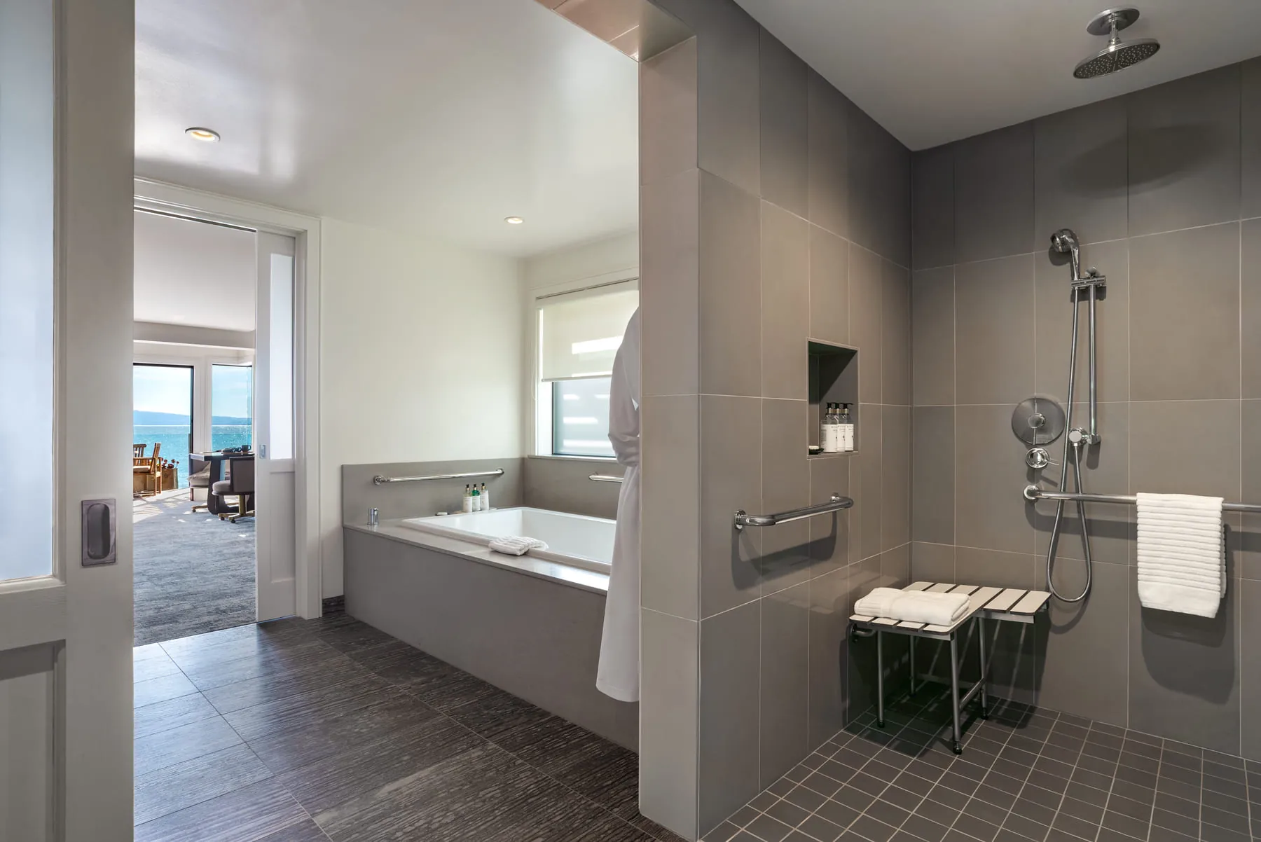 Suite bathroom with walk-in tiled shower, soaking tub, and bay view through doorway