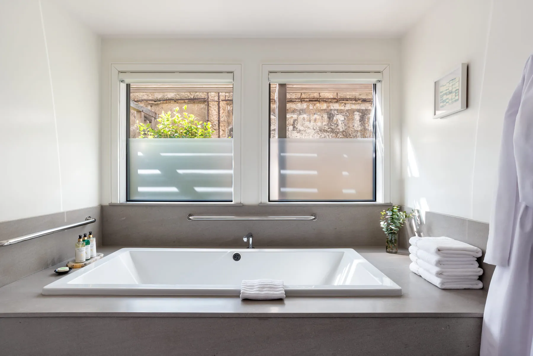 Bright suite bathroom with deep soaking tub below frosted windows and stacked towels